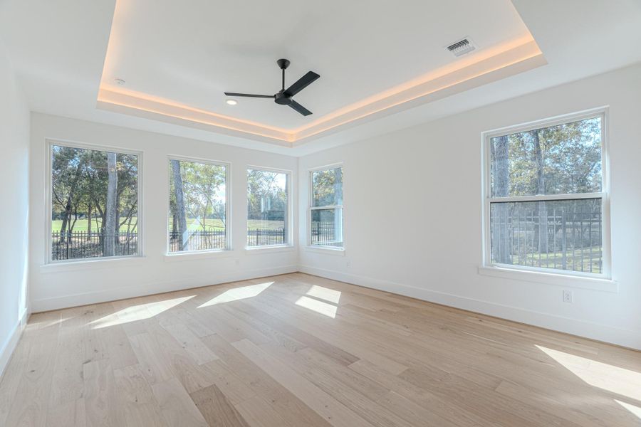 Bright and spacious room with large windows offering a scenic view of trees. Features light wood flooring, recessed ceiling lighting, and a modern ceiling fan. Ideal for a living or dining area.