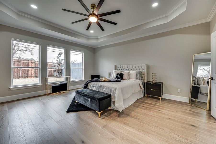 Bedroom with a raised ceiling, ornamental molding, ceiling fan, and light hardwood / wood-style flooring