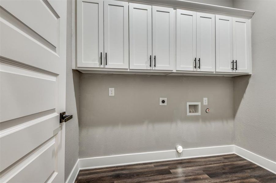 Washroom featuring hookup for a gas dryer, hookup for a washing machine, electric dryer hookup, cabinet space, and dark wood-style flooring Washroom featuring hookup for a gas dryer, hookup for a washing machine, electric dryer hookup, cabinet space, and dark wood-style flooring