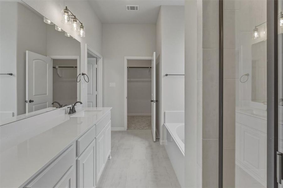 Bathroom featuring a dual vanity with white cabinetry and countertops, a large mirror, and a five-light vanity fixture Bathroom featuring a dual vanity with white cabinetry and countertops, a large mirror, and a five-light vanity fixture