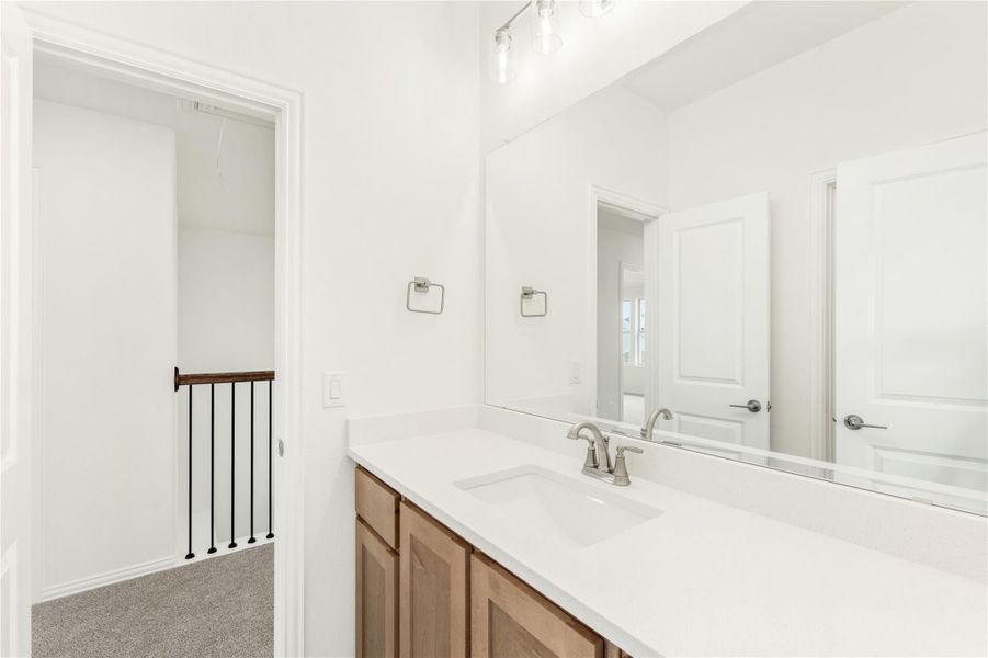 Bathroom vanity with wood cabinets, white countertop, single sink, and large mirror with overhead lighting.