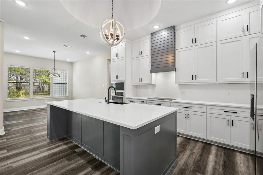 Kitchen with sink, hanging light fixtures, an island with sink, white cabinets, and dark wood-type flooring