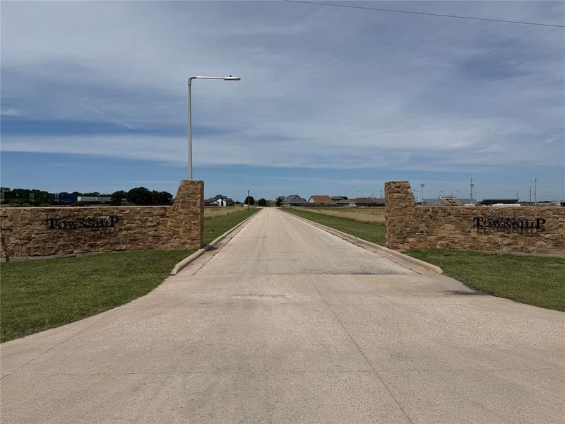 Stone entry monuments flank the paved road, featuring integrated street lighting and manicured grass verges