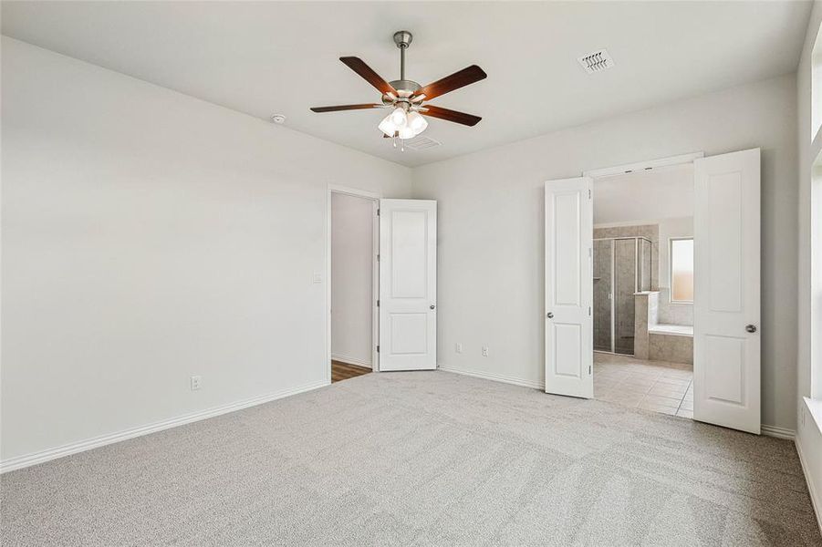 Unfurnished bedroom featuring light carpet, connected bathroom, and ceiling fan