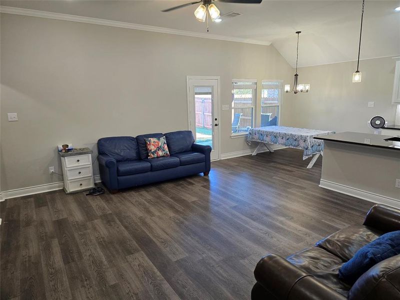 Living room featuring ceiling fan with notable chandelier, crown molding, dark hardwood / wood-style flooring, and lofted ceiling