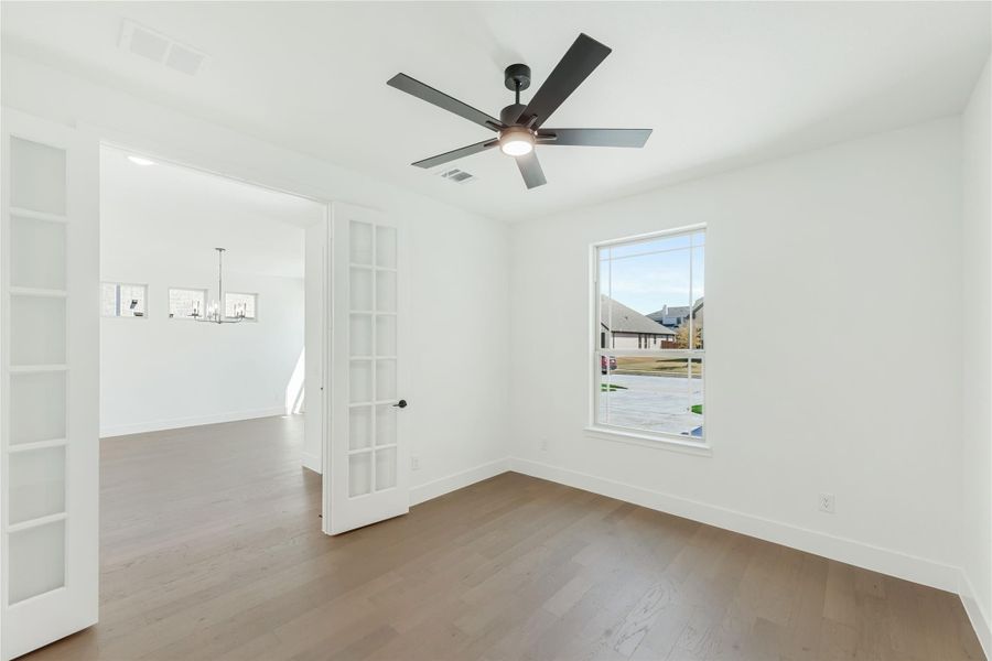 Empty room with hardwood floors, ceiling fan, and French doors leading to dining area