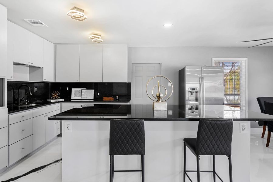 Kitchen featuring stainless steel refrigerator with ice dispenser, white cabinets, a breakfast bar area, backsplash, and dark stone counters