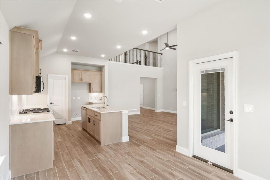 Open kitchen with light wood cabinets, center island, high ceilings, and wood-look tile floors leading to living area