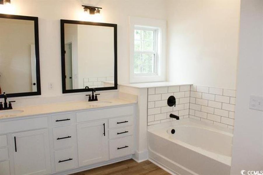 Bathroom featuring double vanity, a bath, and light wood-style flooring
