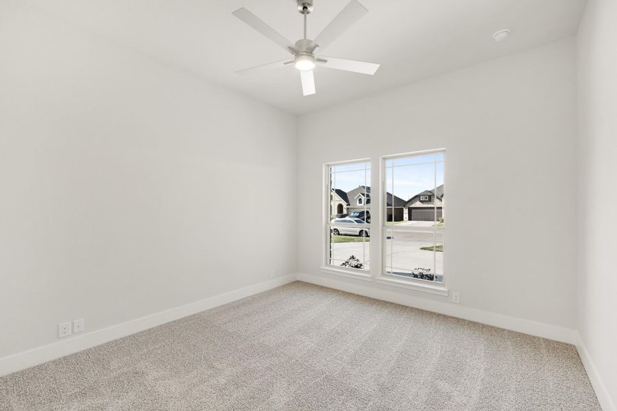 Empty bedroom with ceiling fan, carpet flooring, and two windows overlooking a neighborhood street. Empty bedroom with ceiling fan, carpet flooring, and two windows overlooking a neighborhood street.