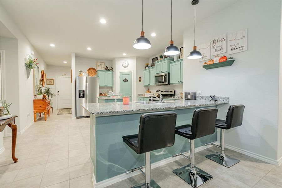 Kitchen with a peninsula, a sink, stainless steel appliances, green cabinets, and a kitchen breakfast bar