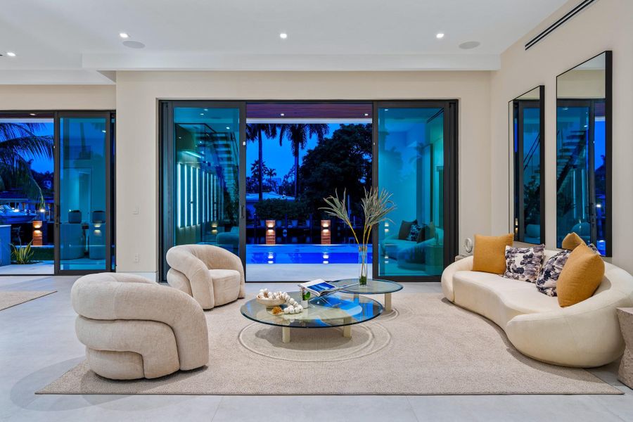 Stylish living room with designer furnishings and expansive glass doors opening to the illuminated pool and waterfront views. Stylish living room with designer furnishings and expansive glass doors opening to the illuminated pool and waterfront views.