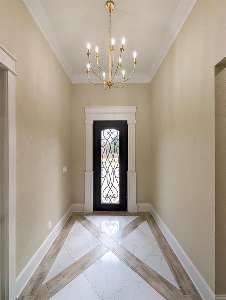 Entryway with a chandelier, inlaid floor details, a textured wall, crown molding, and light marble finish floors