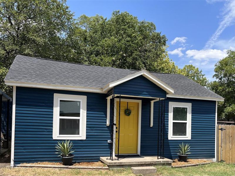 Charming single-story exterior featuring deep blue horizontal siding, a contrasting yellow front door, and a dark asphalt shingle roof