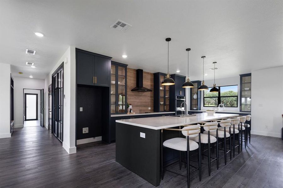 Gourmet kitchen featuring a large island with seating, dark cabinetry, wood-finish flooring, recessed lighting, and a large window Gourmet kitchen featuring a large island with seating, dark cabinetry, wood-finish flooring, recessed lighting, and a large window