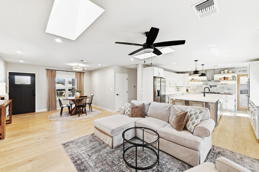 Living room featuring light wood-style flooring, ceiling fan, a skylight, and recessed lighting