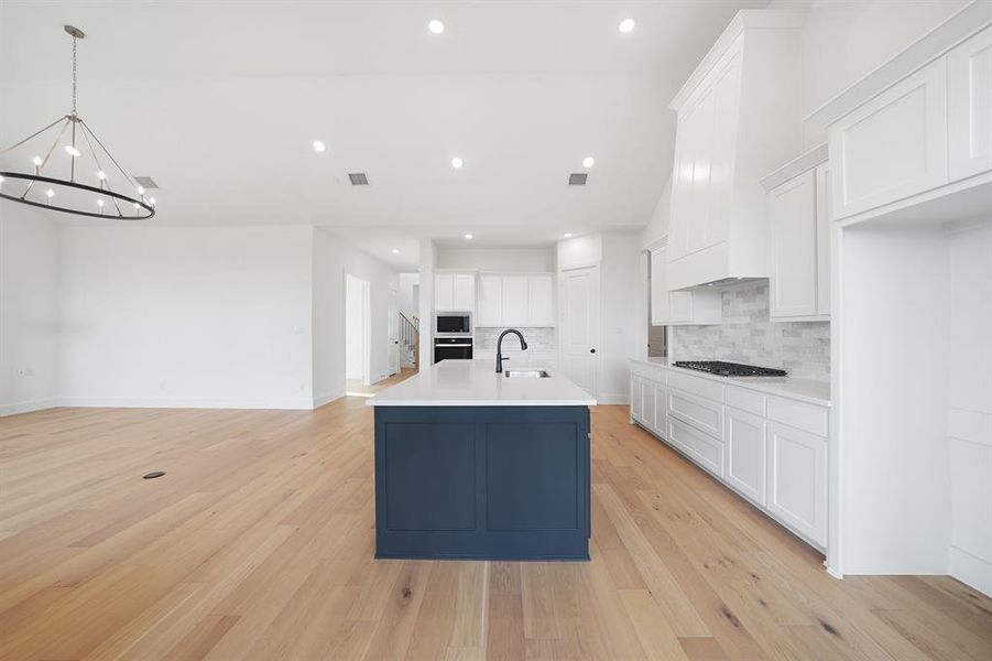Kitchen with white cabinetry, an island with sink, light wood finished floors, decorative backsplash, and recessed lighting