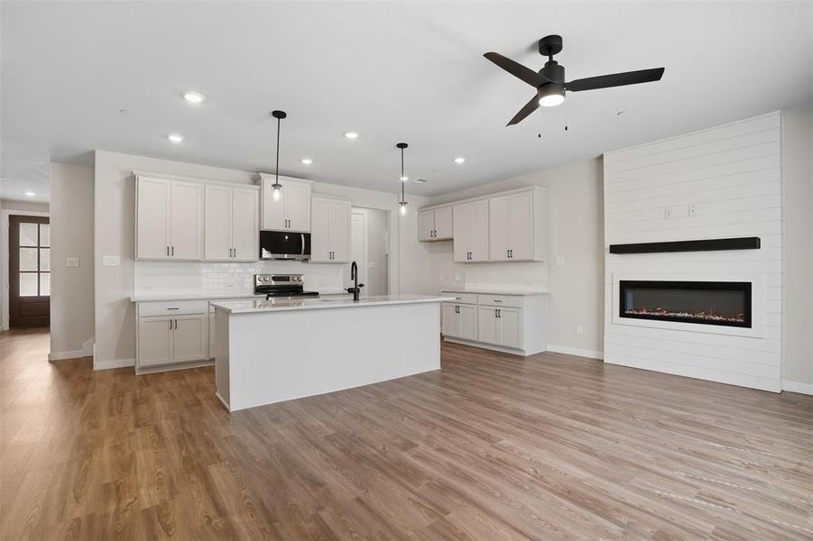 Kitchen featuring white cabinetry, decorative light fixtures, light wood finished floors, a center island with sink, and recessed lighting Kitchen featuring white cabinetry, decorative light fixtures, light wood finished floors, a center island with sink, and recessed lighting