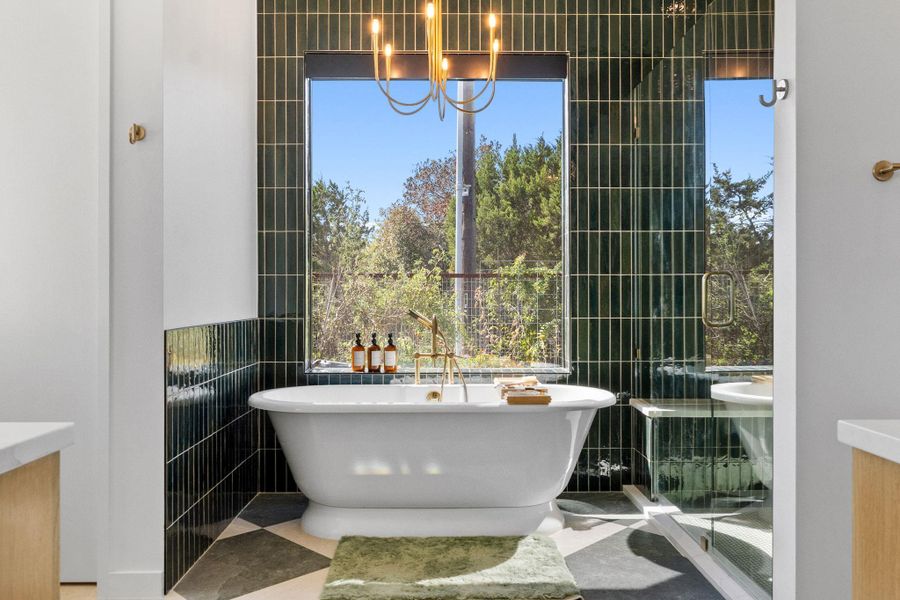 Freestanding soaking tub with brass fixtures, set against a dark green vertical tile accent wall