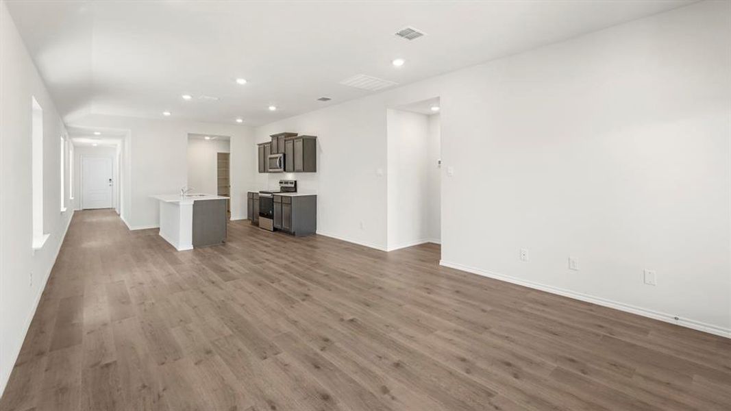 Open-concept living space featuring wood-finish flooring, recessed lighting, and a modern kitchen island with an integrated sink
