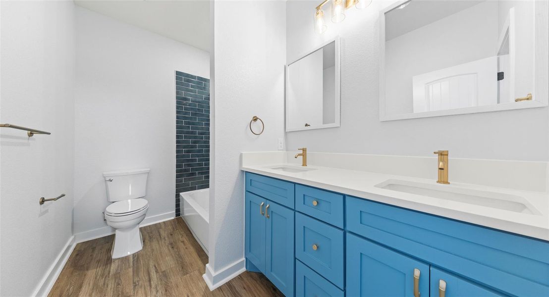 Full bath with double vanity, tub / shower combination, and dark wood-style flooring