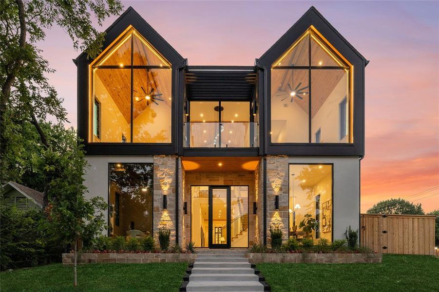 Modern facade featuring expansive glazing, stone accents, a second-story balcony with glass railings, and a prominent peaked roofline Modern facade featuring expansive glazing, stone accents, a second-story balcony with glass railings, and a prominent peaked roofline