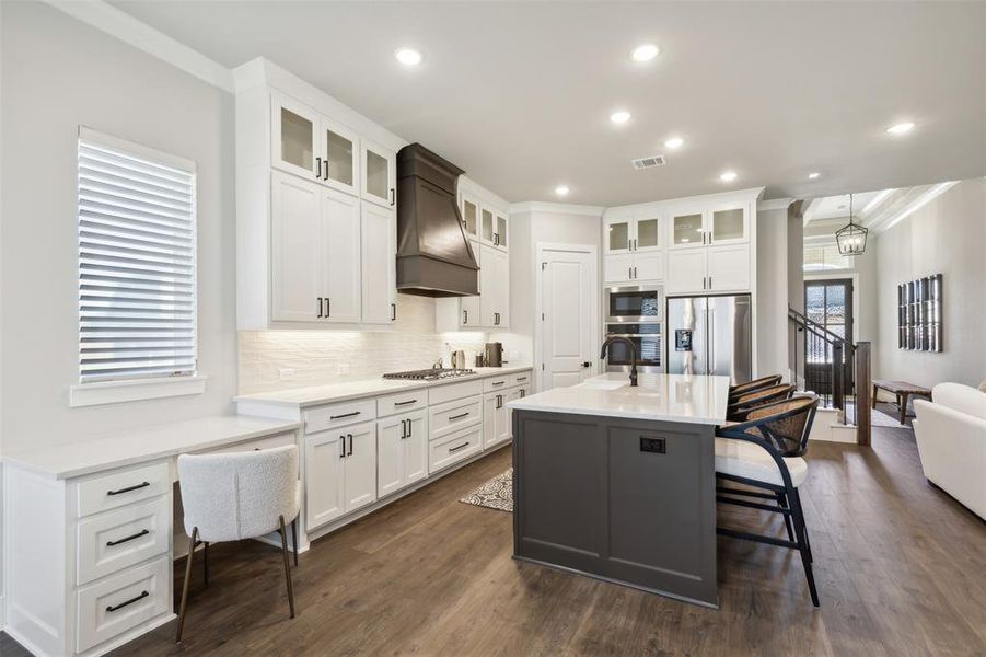 Kitchen featuring appliances with stainless steel finishes, custom exhaust hood, dark wood-type flooring, crown molding, and an island with sink