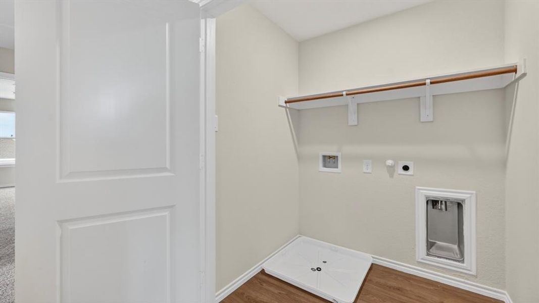 Dedicated laundry area featuring wood-finish flooring, a white utility basin, a garment hanging rod, and wall-mounted shelving