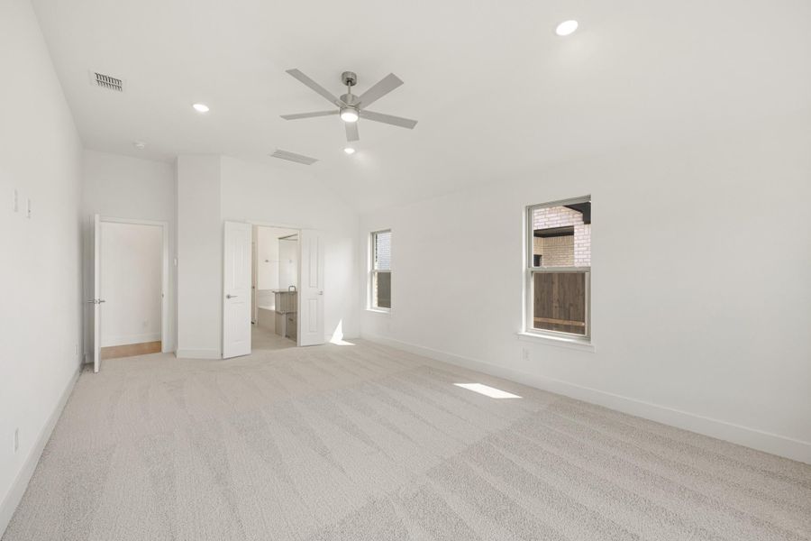Spacious empty bedroom with carpet, ceiling fan, high ceilings, and an open door to an ensuite bathroom