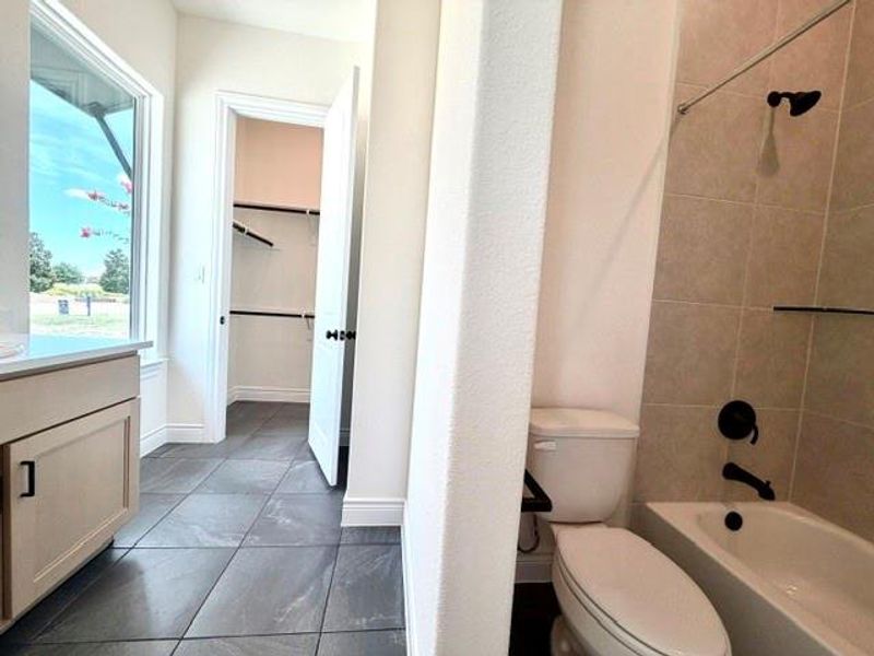 A well-lit primary bathroom featuring sleek tile flooring and a functional walk-in closet. A well-lit primary bathroom featuring sleek tile flooring and a functional walk-in closet.