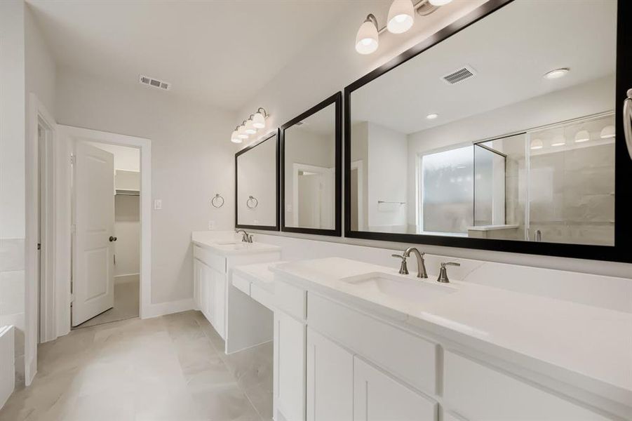 Spacious bathroom featuring a double vanity with white countertops, undermount sinks, brushed nickel fixtures, and individual framed mirrors