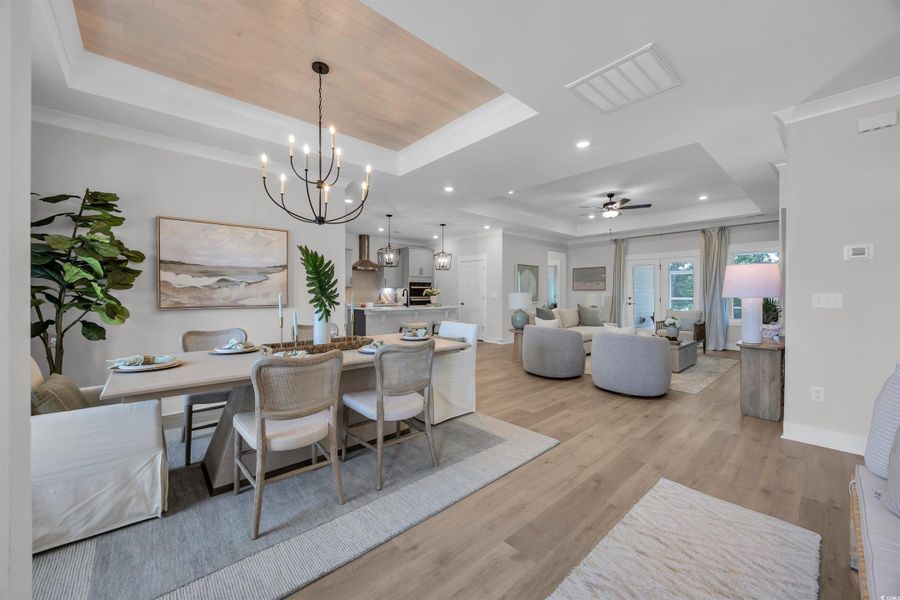 Dining space with a tray ceiling, ornamental molding, light wood-style flooring, ceiling fan, and a chandelier