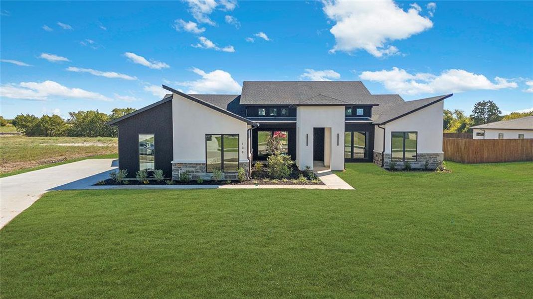 Modern architectural exterior featuring a striking black and white facade, large windows, a contrasting stone base, a dark shingle roof, and a concrete driveway Modern architectural exterior featuring a striking black and white facade, large windows, a contrasting stone base, a dark shingle roof, and a concrete driveway