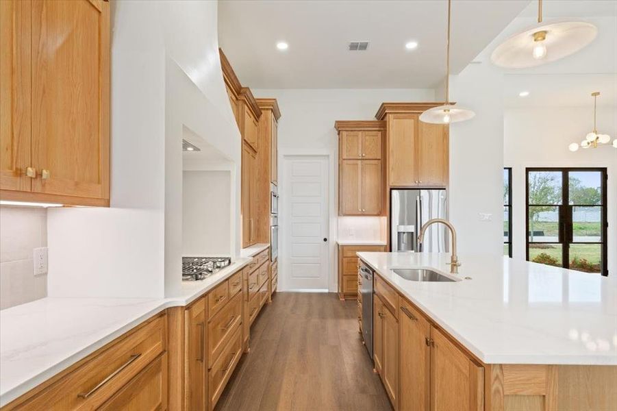 Kitchen featuring a center island with sink, dark wood-style flooring, light stone counters, pendant lighting, and stainless steel appliances