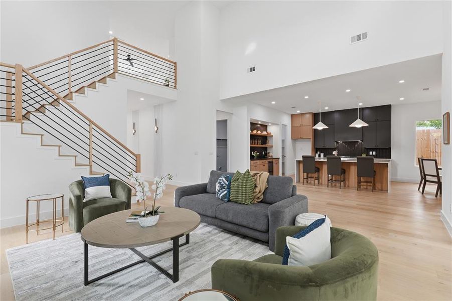 Double-height living space featuring light wood-finish flooring, a contemporary staircase with wood and metal railings, and recessed lighting Double-height living space featuring light wood-finish flooring, a contemporary staircase with wood and metal railings, and recessed lighting
