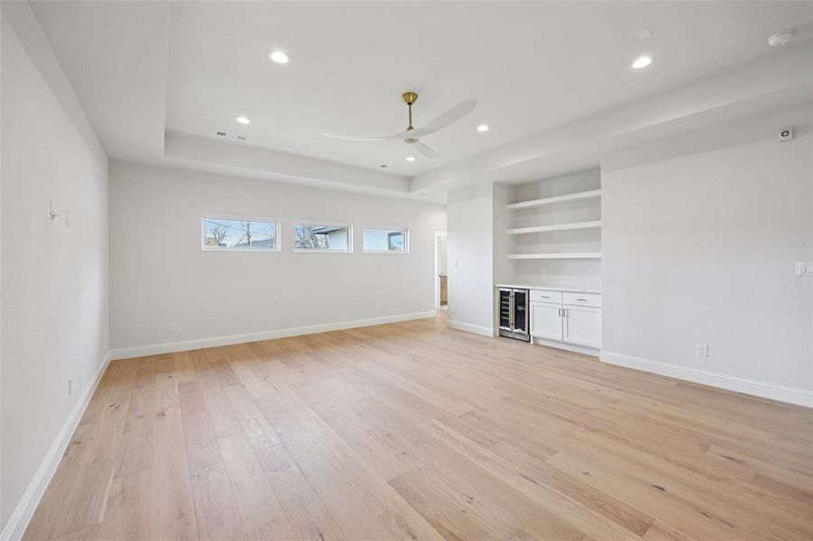 Unfurnished living room with light wood finished floors, wine cooler, built in features, recessed lighting, and ceiling fan