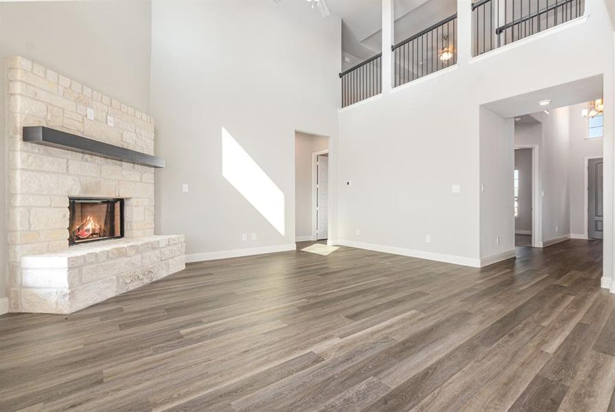 Unfurnished living room featuring wood finished floors, a stone fireplace, and a high ceiling