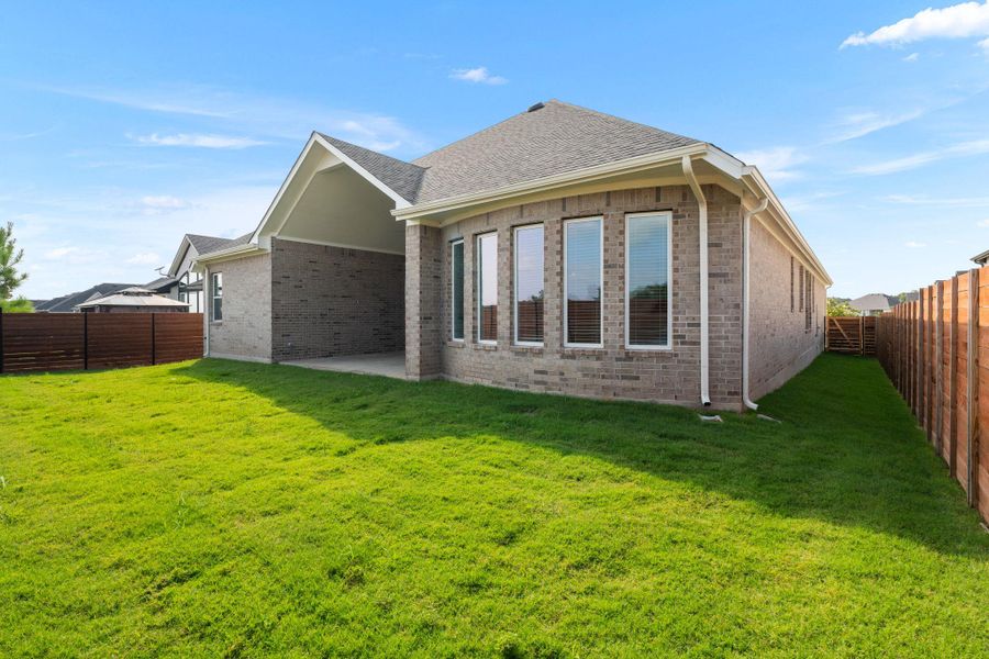 A well-maintained lawn stretches beside a contemporary brick residence featuring a covered patio and a privacy fence.