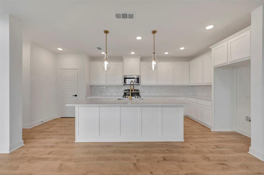 Kitchen featuring white cabinets, a center island with sink, and light wood-style flooring