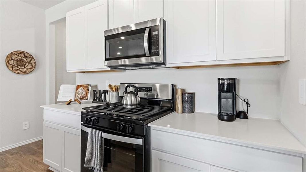 Kitchen featuring white cabinetry, light-toned countertops, a stainless steel microwave, a black gas range, and wood-finish flooring