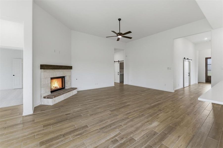This expansive open-concept living area features wood-look tile flooring, a fireplace with a stone surround and brick hearth, and a ceiling fan