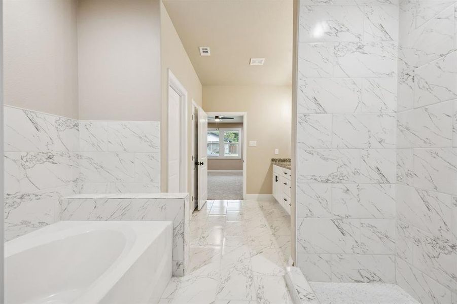 Bathroom featuring tile walls, a garden tub, vanity, and light marble finish floors Bathroom featuring tile walls, a garden tub, vanity, and light marble finish floors