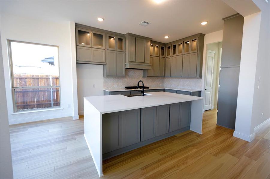 Kitchen with a center island with sink, light stone counters, gray cabinets, light wood finished floors, and recessed lighting Kitchen with a center island with sink, light stone counters, gray cabinets, light wood finished floors, and recessed lighting
