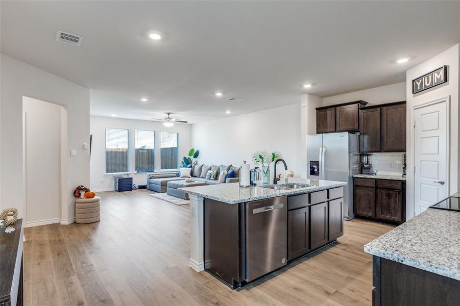 Kitchen with dark brown cabinetry, light stone countertops, an island with sink, light wood-style flooring, and recessed lighting Kitchen with dark brown cabinetry, light stone countertops, an island with sink, light wood-style flooring, and recessed lighting