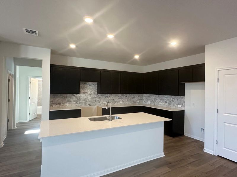 Kitchen with dark wood-style flooring, backsplash, an island with sink, recessed lighting, and light stone countertops Kitchen with dark wood-style flooring, backsplash, an island with sink, recessed lighting, and light stone countertops