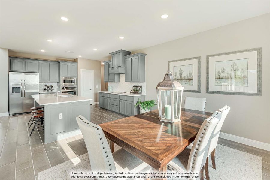 Open dining area with wood table and upholstered chairs adjoining kitchen with gray cabinets and stainless appliances