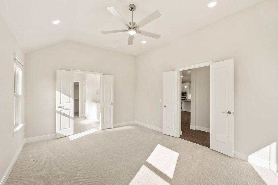 Empty bedroom with vaulted ceiling, ceiling fan, carpet flooring, and doors leading to closet and bathroom