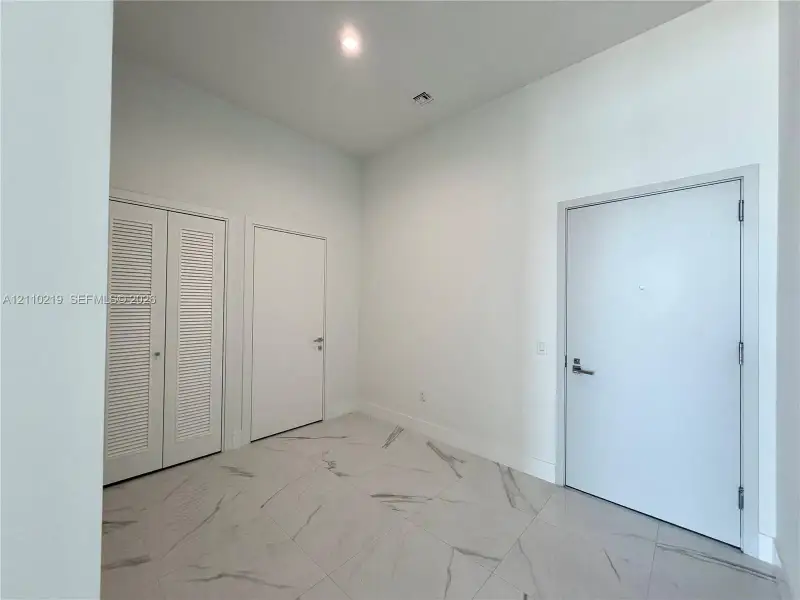 High-ceiling entryway featuring large-format tile flooring with marble-pattern veining, recessed lighting, and white louvered closet doors