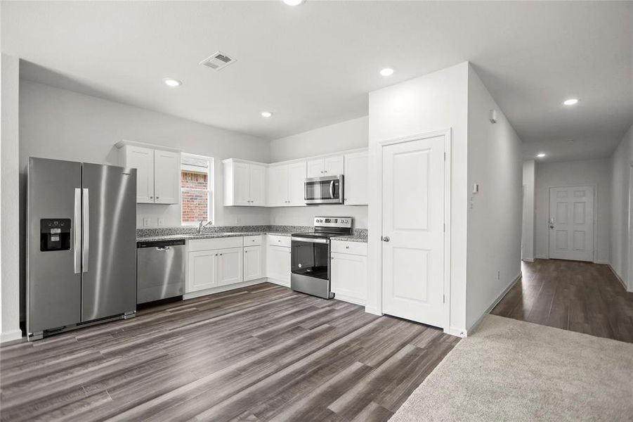 Kitchen featuring white cabinetry, stainless steel appliances, speckled countertops, and wood-finish flooring