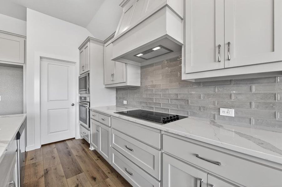 Contemporary kitchen featuring light gray cabinetry, built-in stainless steel appliances, a flush-mount cooktop, and a subway tile backsplash